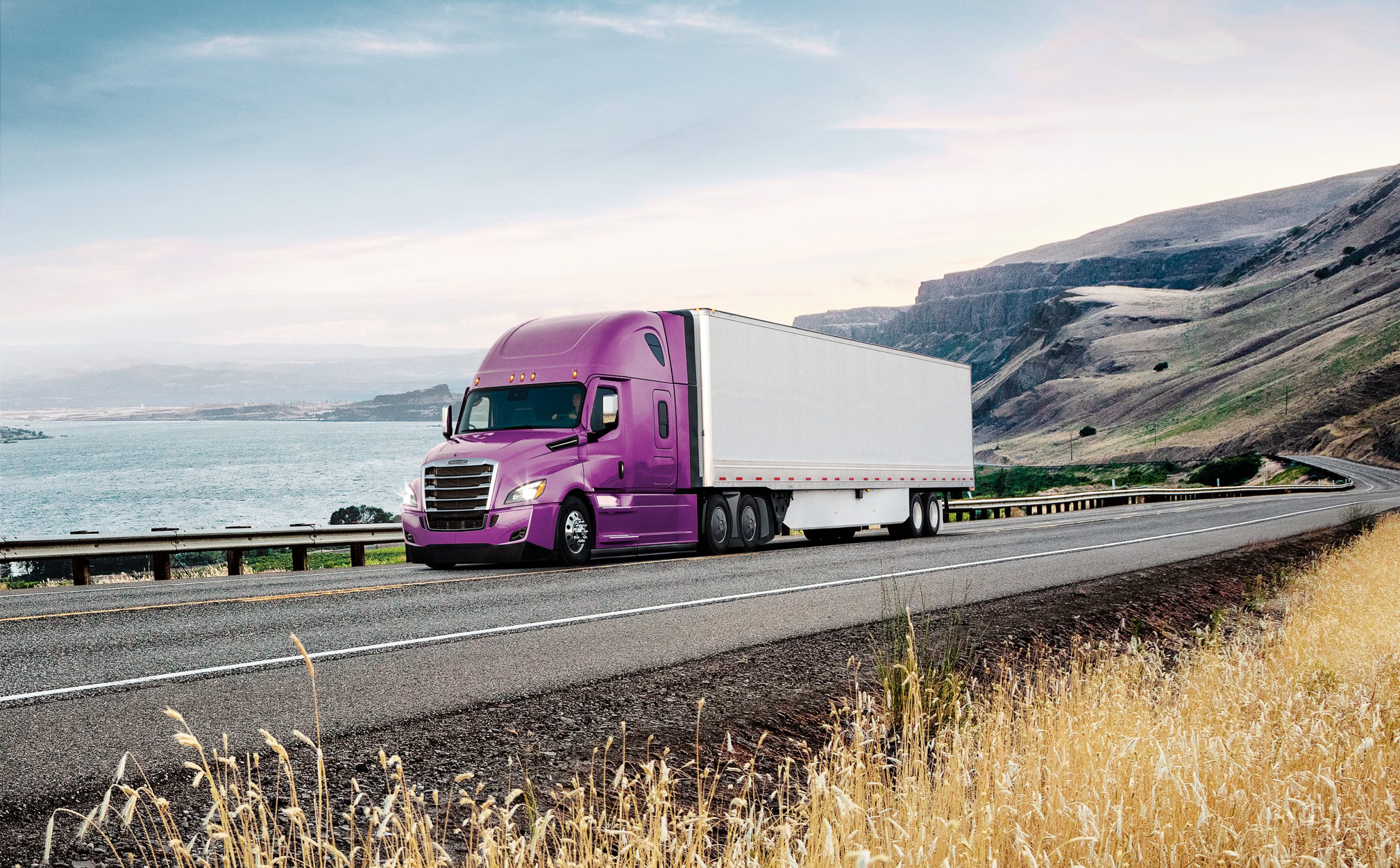 Photo of Freightliner truck driving on highway that is alongside a body of water.